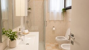 Een moderne badkamer met een douchecabine van glas, een wastafel met spiegel, een toilet en een plant in pot.