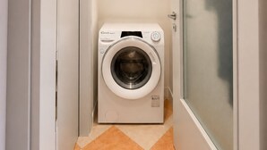 Een kleine wasruimte met een voorlader wasmachine, betegelde vloer en een deur met ruitverdeling.