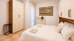 Een slaapkamer met een bed, een kledingkast, een radiator, een schilderij en een klein tafeltje.