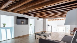 Een ruime woonruimte met houten balken, een flatscreen televisie, een tafel en een bank.