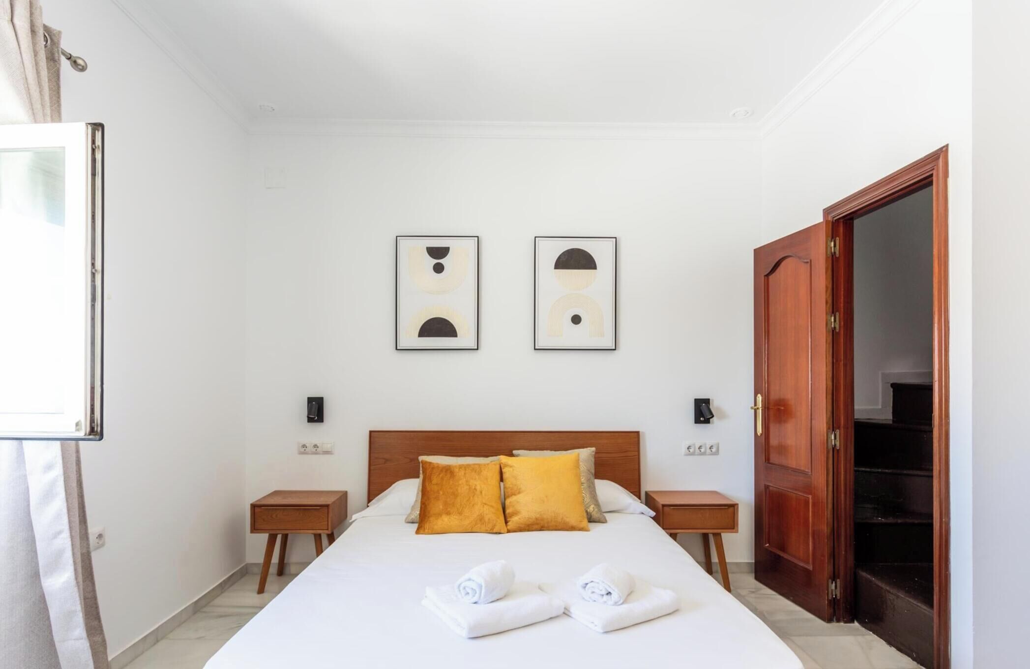 Une chambre d’hôtel comprenant un lit, deux tables de chevet, une armoire en bois et deux œuvres d’art abstraites accrochées au mur.