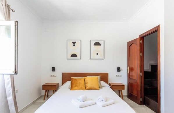 Une chambre d’hôtel comprenant un lit, deux tables de chevet, une armoire en bois et deux œuvres d’art abstraites accrochées au mur.
