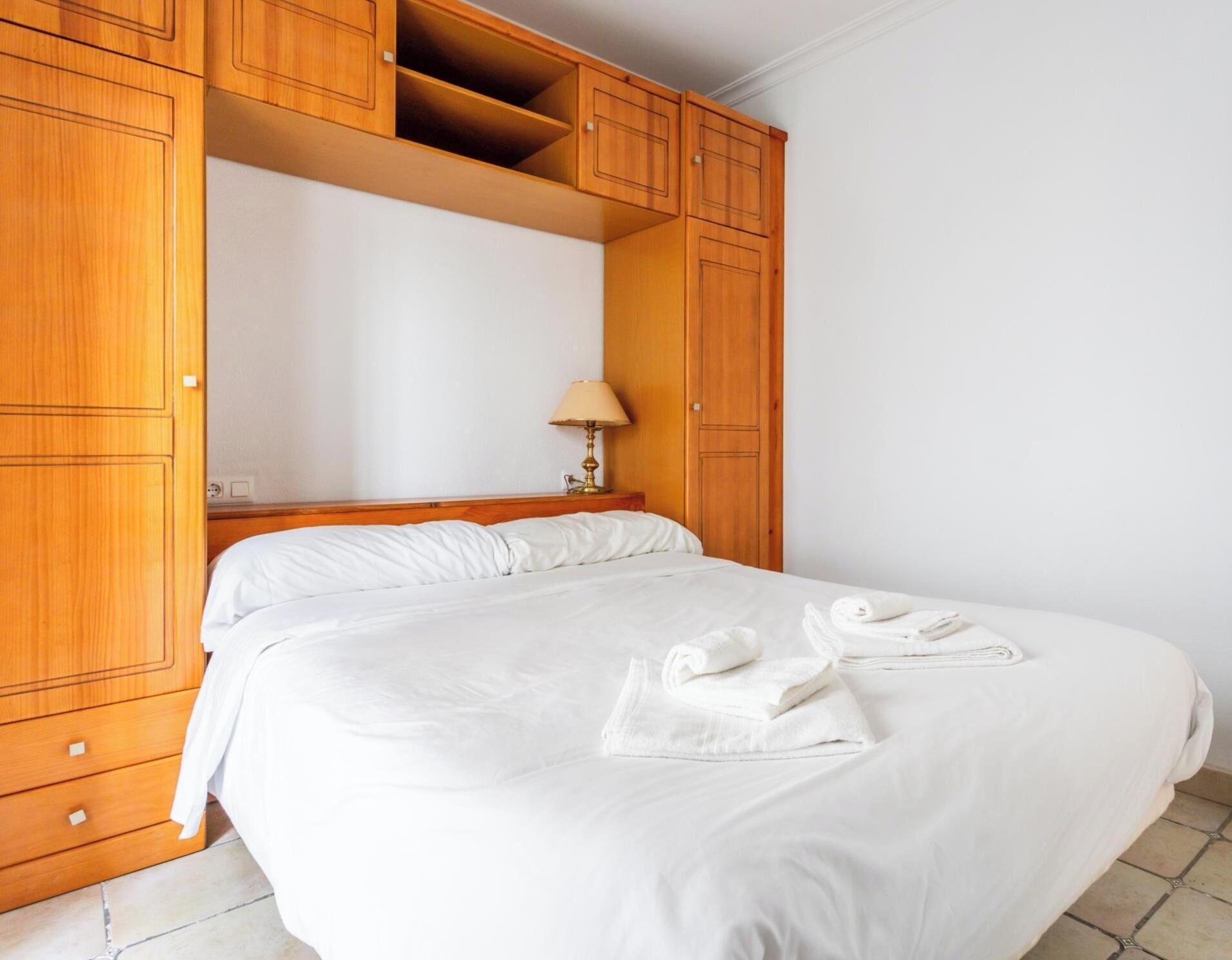 Habitación de hotel con una cama grande, armario de madera y una lámpara de noche.