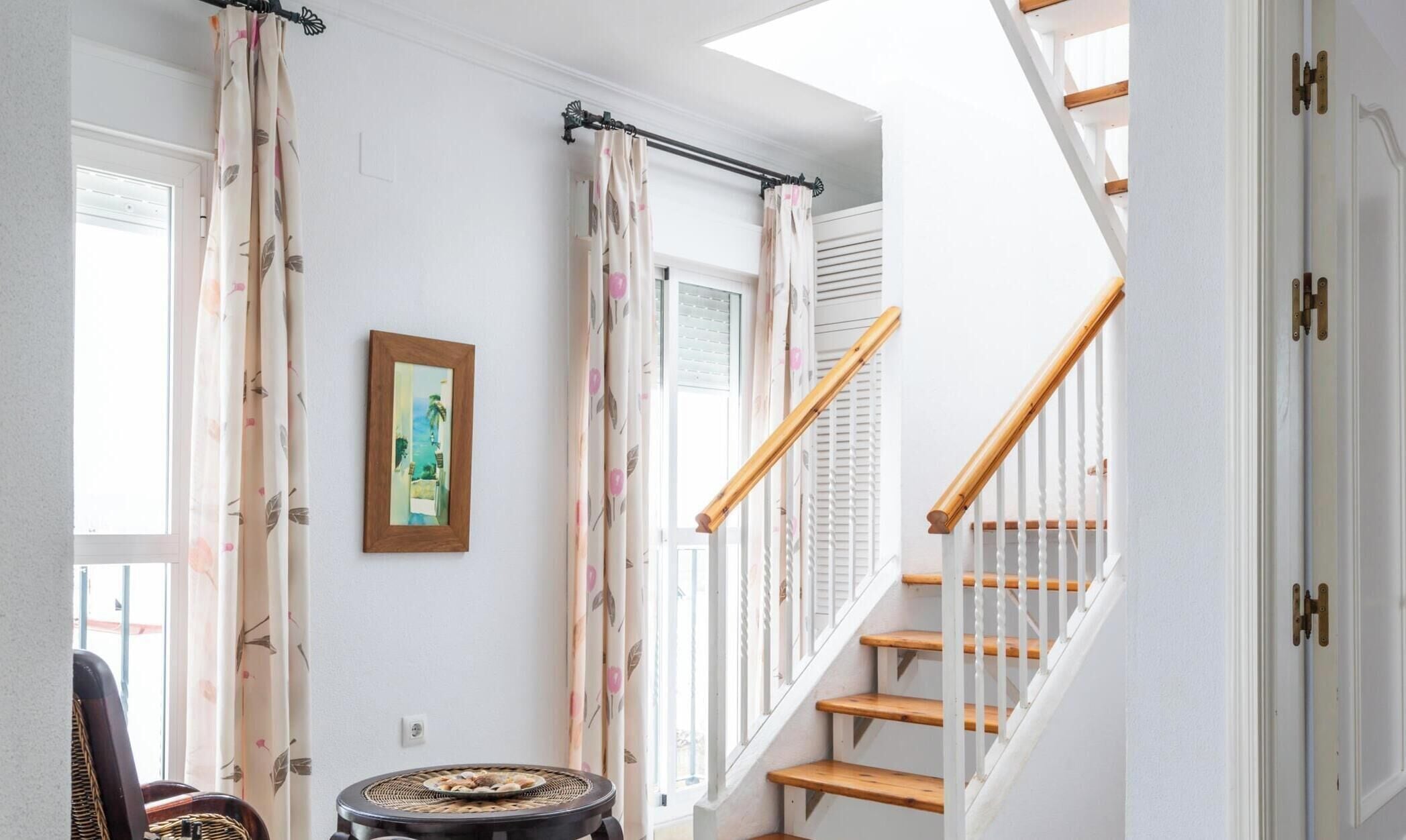 A staircase with wooden steps and white railings, a framed painting on the wall, and a woven basket on the floor.