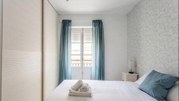 Une chambre d’hôtel avec un lit, une table de chevet, une lampe et une fenêtre avec des rideaux.