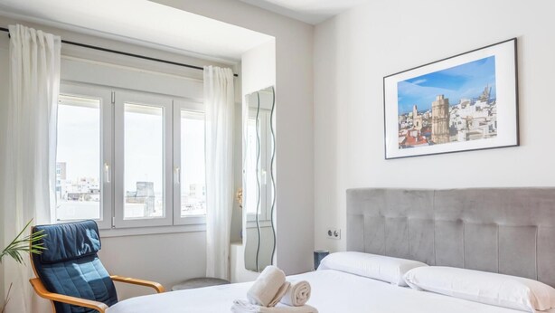 Ein Hotelzimmer mit Bett, Sessel, Stadtbildgemälde und einem Vorhangfenster.