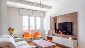 Ein modernes Wohnzimmer mit einer Couch, zwei orangefarbenen Sesseln, einem Fernseher und einer Holzkommode.