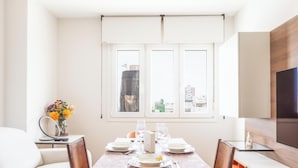 Ein Essbereich mit einem Tisch für vier Personen, einer Blumenvase und Blick auf die Stadt durch das Fenster.