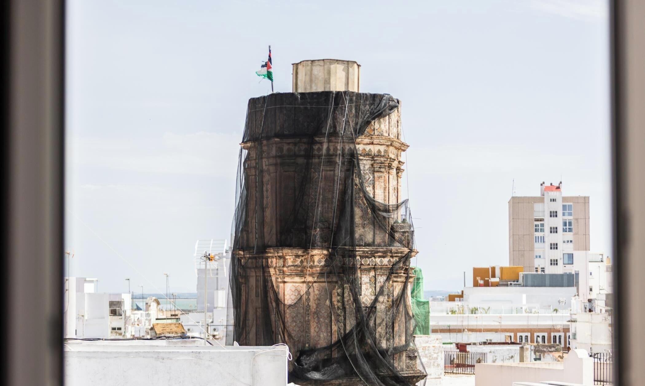 Une haute structure cylindrique surmontée d’un drapeau, entourée de bâtiments modernes.