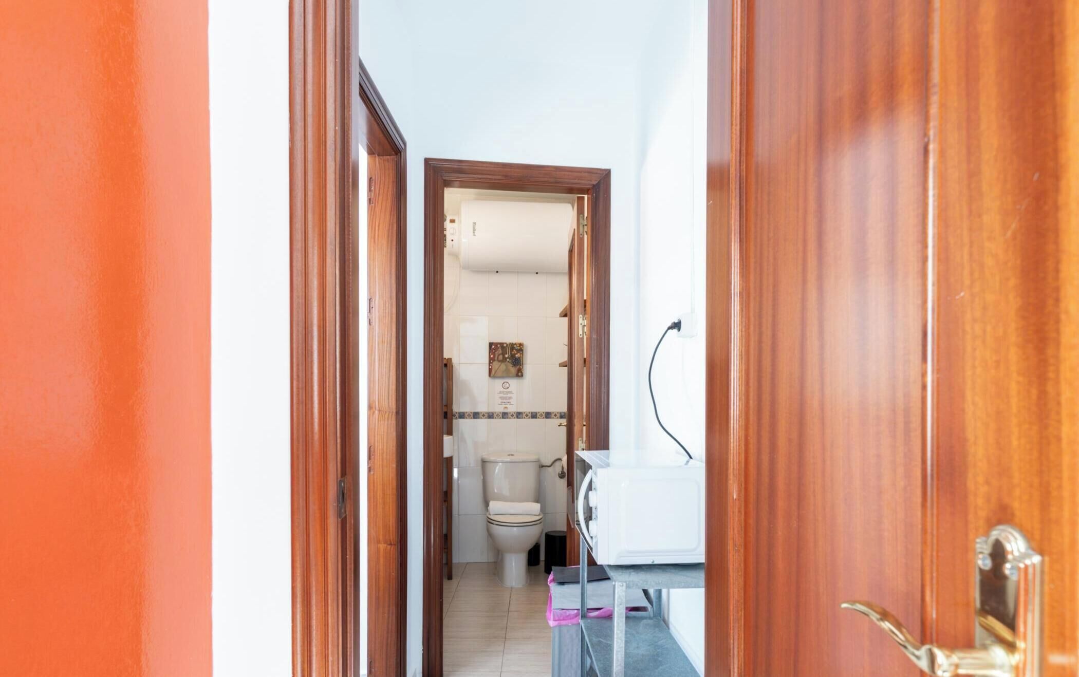 Een gang die leidt naar een badkamer met een toilet, een wastafel en een douchehoek.
