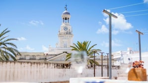 A white tower with a clock, surrounded by palm trees and a clear sky. - Charming Penthouse in the Heart of Cádiz (Ciudad de Cádiz)
