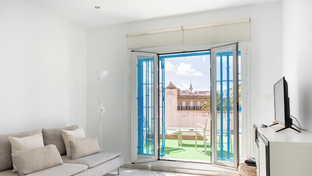 A modern living room with a sofa, a TV, and a view of a courtyard through a large glass door. - Charming Penthouse in the Heart of Cádiz (Ciudad de Cádiz)