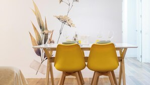 Een eethoek met een tafel gedekt voor twee personen, met gele stoelen en een vaas met gedroogde bloemen.