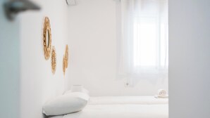 Een witte kamer met een bed, een raam met transparante gordijnen en decoratie aan de muur.