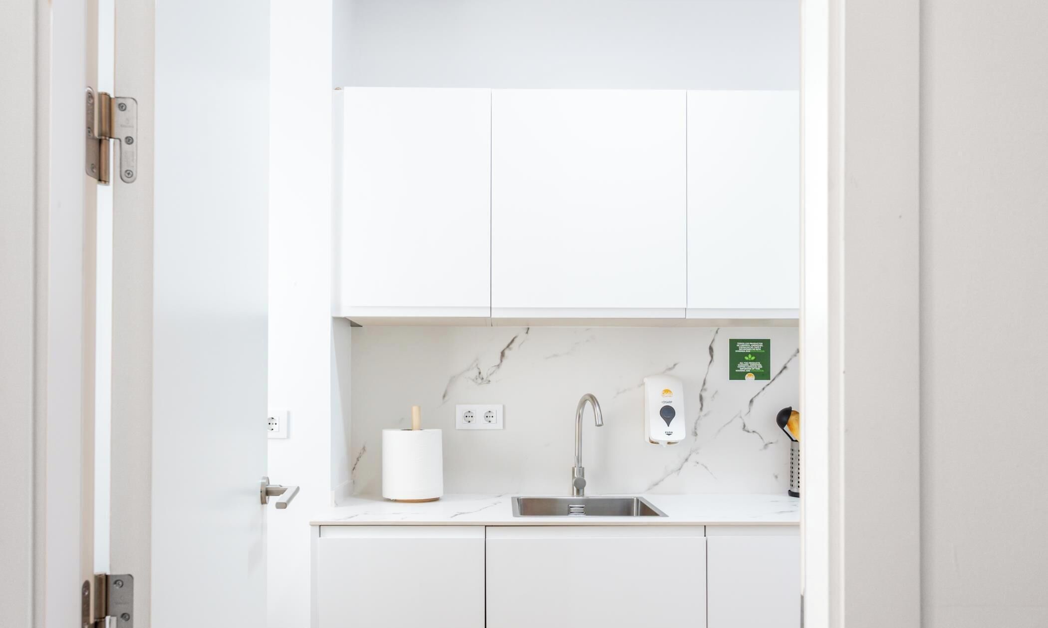 A modern kitchen with white cabinets, a marble backsplash, a stainless steel sink, and a soap dispenser.