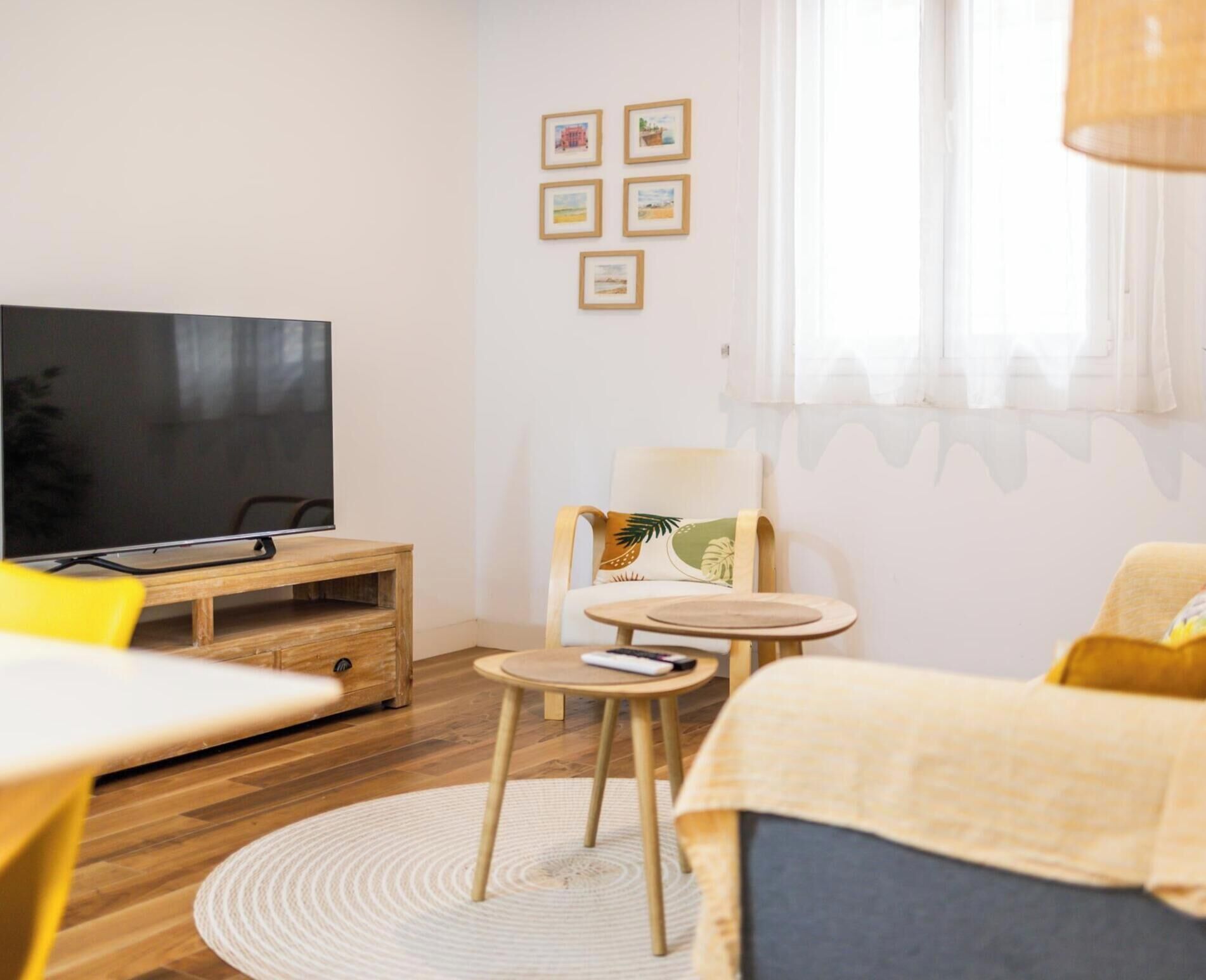 A room with a TV, wooden furniture, a round rug, a chair with a leaf pillow, and framed pictures on the wall.