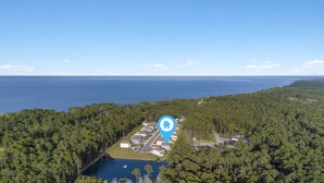 Ilmakuva asuinalueesta, jonka yhteydessä on järvi, ja aluetta ympäröi tiheä metsä. Näköala merelle on avoin ja selkeä.