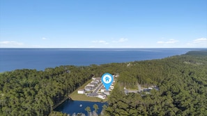 Eine Luftaufnahme eines Wohngebiets mit einem See, umgeben von dichtem Wald, und freiem Blick auf den Ozean.