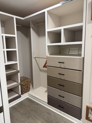Ein begehbarer Kleiderschrank mit offenen Regalen, einer Kleiderstange und Schubladen.