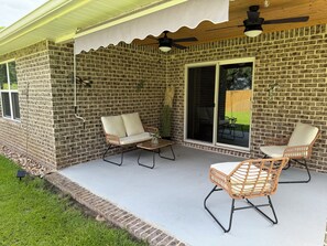 Ein überdachter Patio-Bereich mit Backsteinmauern, zwei Korbstühlen, einem Tisch und Deckenventilatoren.