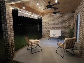 Eine überdachte Terrasse mit Backsteinwänden, zwei Korbstühlen, einem kleinen Tisch und Deckenventilatoren.