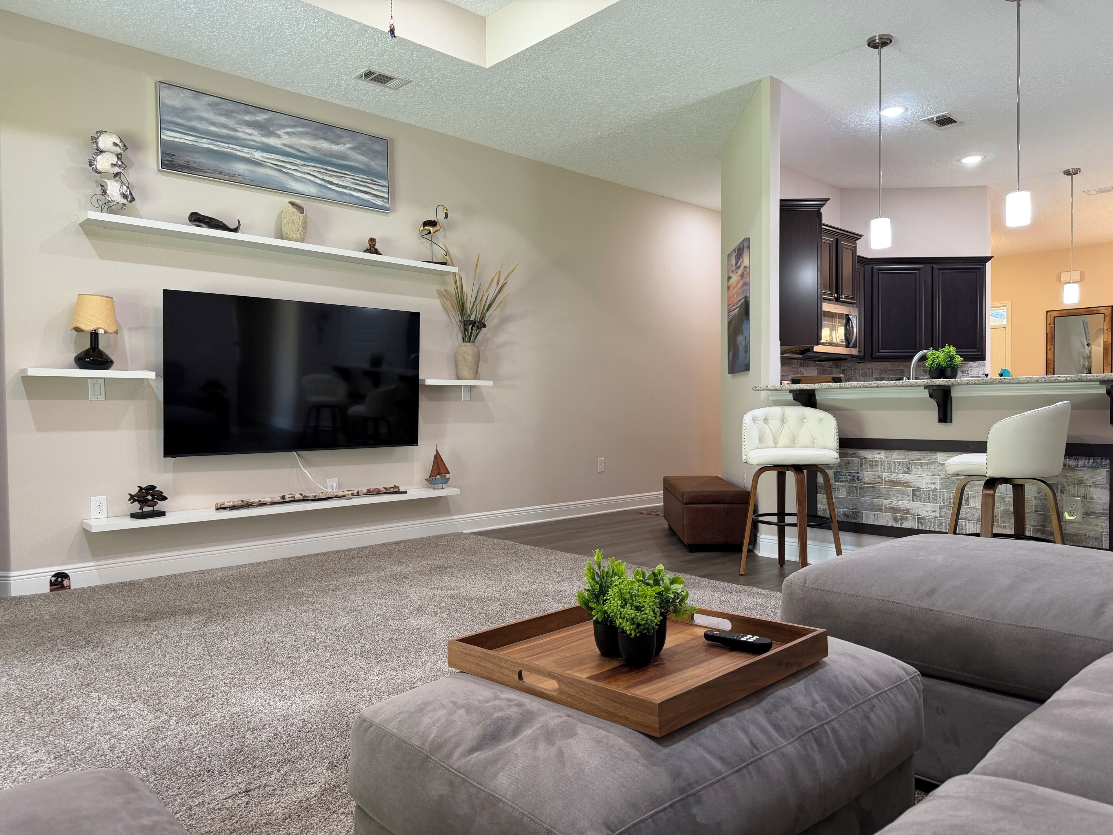 A modern living room with a flat-screen TV, a wooden coffee table with plants, and a grey sofa.