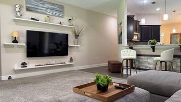 A modern living room with a flat-screen TV, a wooden coffee table with plants, and a grey sofa.
