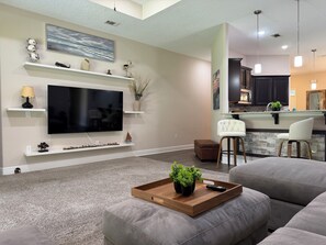 A modern living room with a flat-screen TV, a wooden coffee table with plants, and a grey sofa. - Dual Master Suites~3min Walk to Water ~Sleeps 12 (Gulf Breeze)