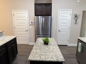 A kitchen with two white doors, a stainless steel refrigerator, dark cabinets, granite countertops, and a small potted plant. - Dual Master Suites~3min Walk to Water ~Sleeps 12 (Gulf Breeze)