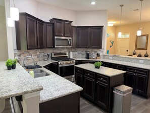 A kitchen with dark cabinets, a stainless steel stove, a microwave, granite countertops, and a trash can. - Dual Master Suites~3min Walk to Water ~Sleeps 12 (Gulf Breeze)