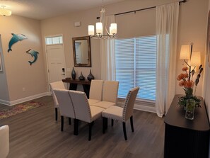 A dining area with a chandelier, a dining table with chairs, decorative wall art, and a window with blinds. - Dual Master Suites~3min Walk to Water ~Sleeps 12 (Gulf Breeze)