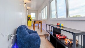 Una habitación con mesa de fútbol de mesa, un sillón de peluche y una mesa con juguetes y juegos.