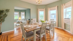 Comedor con una mesa de madera dispuesta para cuatro personas, rodeado de sillas blancas, y un candelabro colgante.