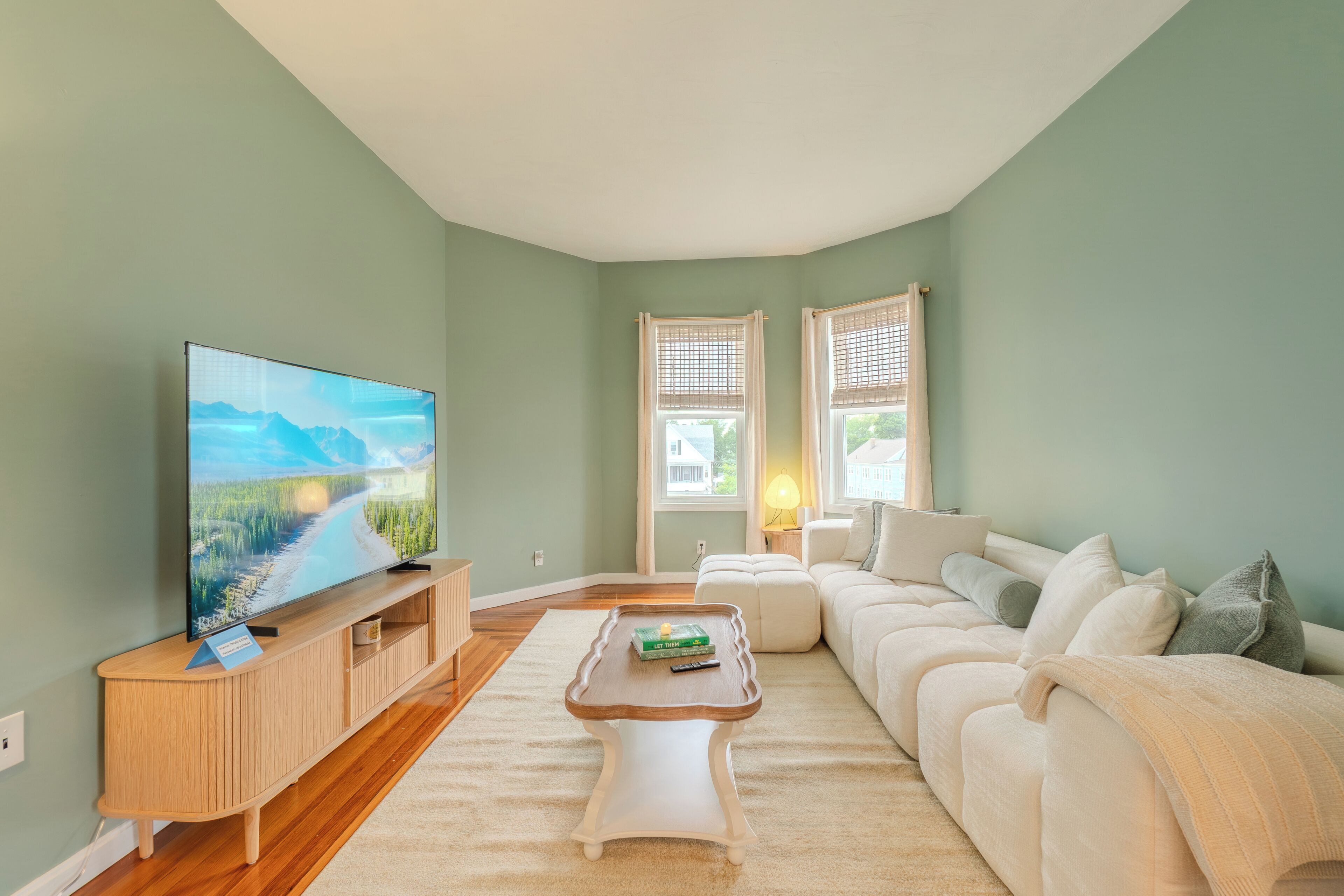 Un salon équipé d’un téléviseur à écran plat, d’un meuble de rangement en bois, d’un canapé blanc et d’une table basse.