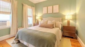 Un dormitorio con cama, mesitas de noche, una ventana con cortinas y decoración en la pared.