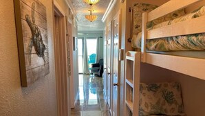 A narrow hallway with bunk beds on one side and a door leading to a room with a view. - Front Row Beachfront Bliss Awaits! Panoramic View! (Galveston)