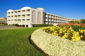 A multi-story hotel with a central courtyard, surrounded by a well-maintained lawn and flower beds. - Front Row Beachfront Bliss Awaits! Panoramic View! (Galveston)