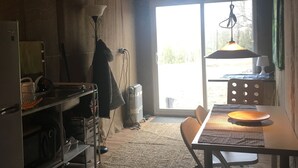 A compact kitchen with a dining table, chairs, a hanging light fixture, and a view through a large window.