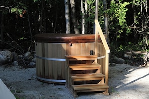 A hot tub with a wooden exterior and a wooden bench with steps leading up to it, surrounded by trees. - Tiny hill top home (Markdale)