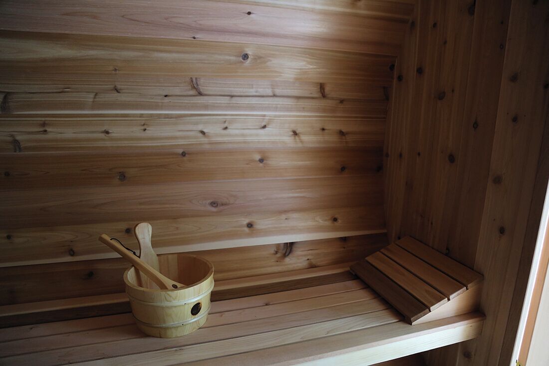 Una sauna de fusta amb una barra i un cubet de fusta amb una cullerada.