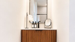 Ein Badezimmer mit Holzwaschtisch, einem Spiegel, drei Pendelleuchten, einem Handtuchhalter und einem schwarz-weißen Schachbrettboden.