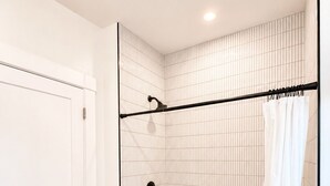 Ein modernes Badezimmer mit einer weißen Badewanne, einer Dusche mit schwarzem Vorhang und einem schwarz-weißen Fußboden.