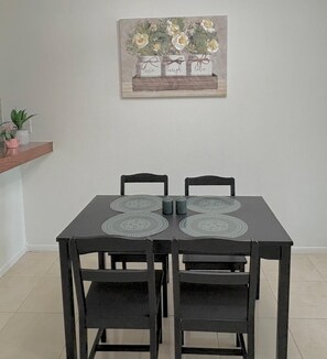 Una mesa de comedor con cuatro sillas, dos individuales y una pequeña planta en maceta sobre una estantería.