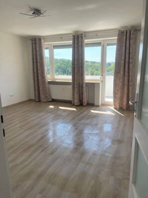 Ein Zimmer mit großem Fenster, Holzboden und Deckenventilator.