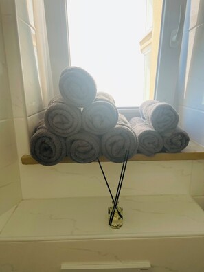 Ein Fenster mit aufgerollten Handtüchern auf einem Regal und einer Glasvase mit einer Kerze.