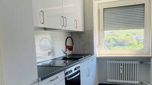 A modern kitchen with white cabinets, a black countertop, a built-in oven, and a window with blinds. - Stylish City Retreat – Your Temporary Home in Würzburg for 7 People (Würzburg)