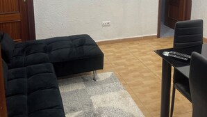 Ein Wohnzimmer mit einem schwarzen Sofa, einem kleinen Tisch mit einer Fernbedienung und zwei Bildern an der Wand.