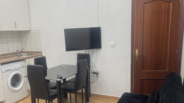 Ein kompakter Wohnraum mit Essbereich, einem an der Wand befestigten Flachbildfernseher, einer Waschmaschine und einer Holztür.