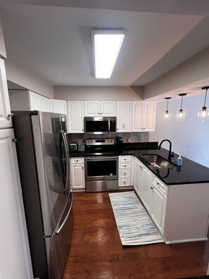 A modern kitchen with stainless steel appliances, white cabinetry, and a black countertop.