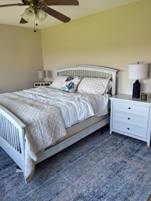 A bedroom with a bed, nightstand, lamp, and ceiling fan.
